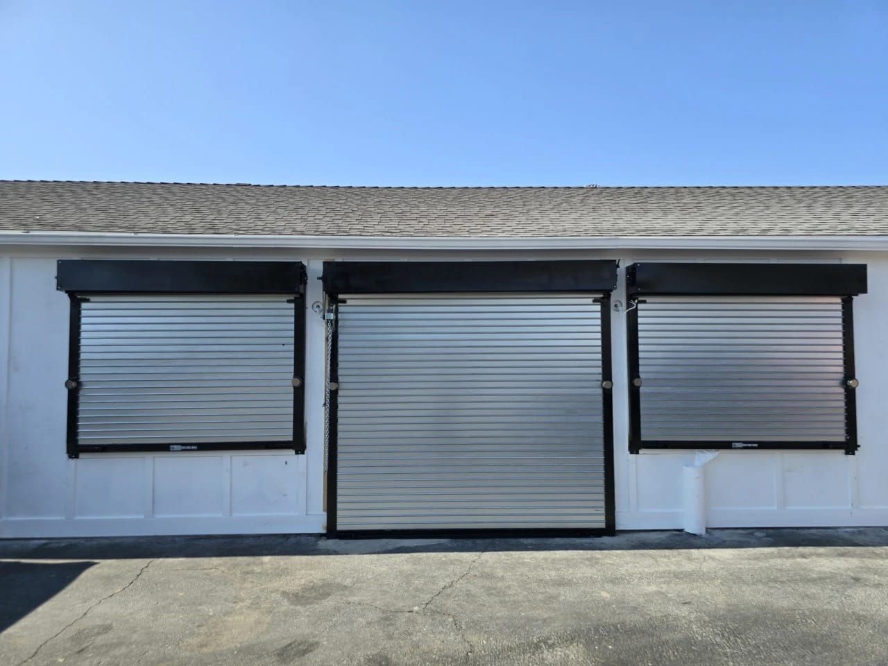 Three closed commercial roll-up doors in a white block wall, a full height truck entry bay between two loading dock doors, each in a black frame
