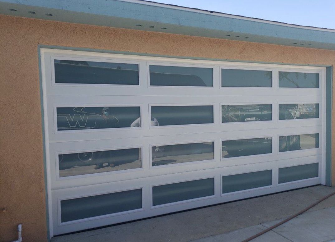 A full-view aluminium garage door with white rails and four rows of frosted glass panels, newly installed on a San Diego home